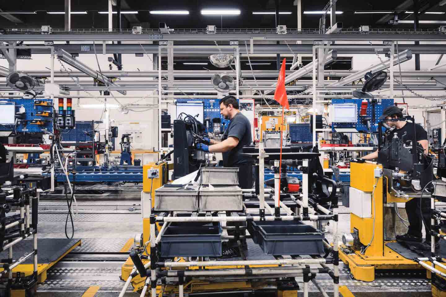 Workers in a modern manufacturing facility operating machinery and assembly lines equipped with various high-tech devices and tools.