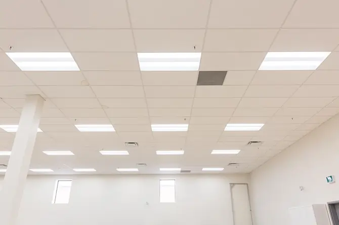 Modern office ceiling with recessed lighting fixtures and white ceiling tiles.