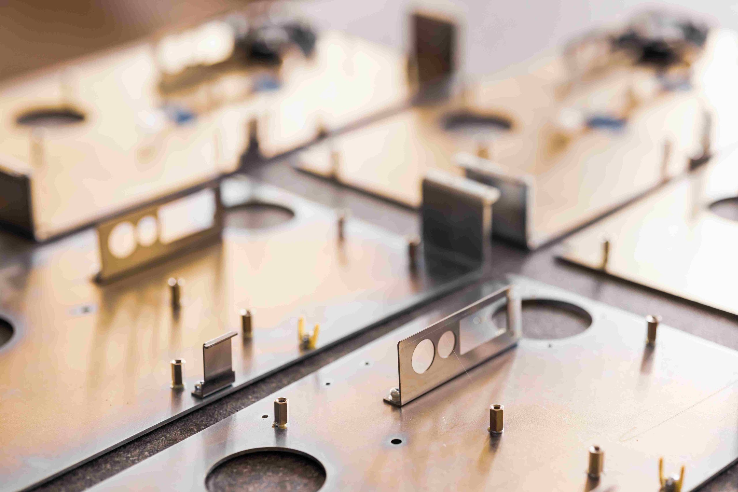 Close-up of metal boards and accessories, including metal brackets and standoffs, laid on a flat surface