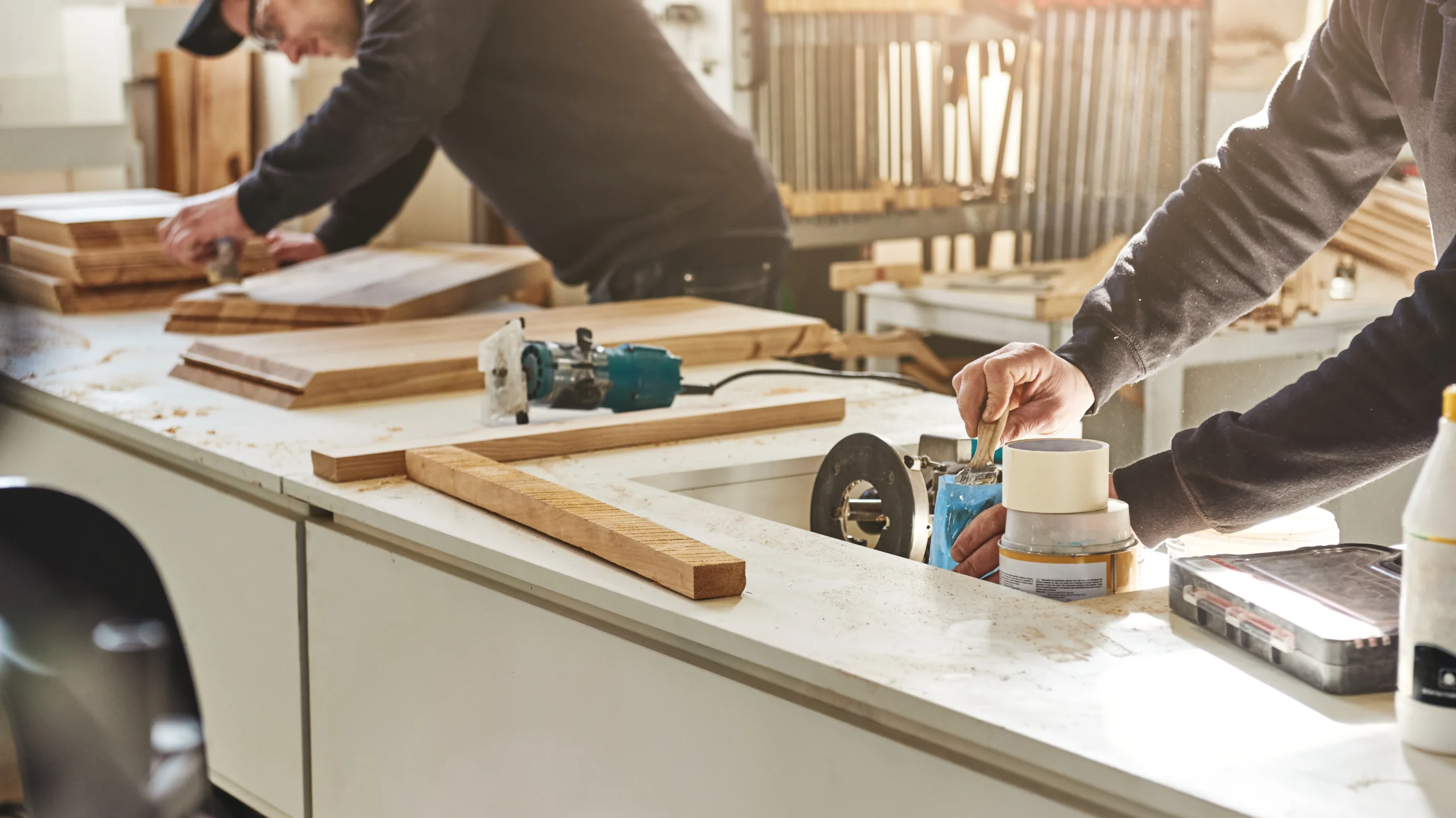 Two craftsmen working in a woodworking shop, sanding and preparing wooden boards with precision tools on a well-organized workstation.